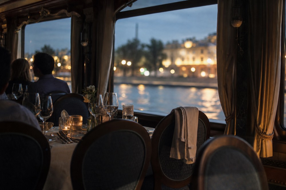 Candlelit dinner cruise table setting on a Budapest boat with the illuminated riverbank outside, no text, no logos, no people