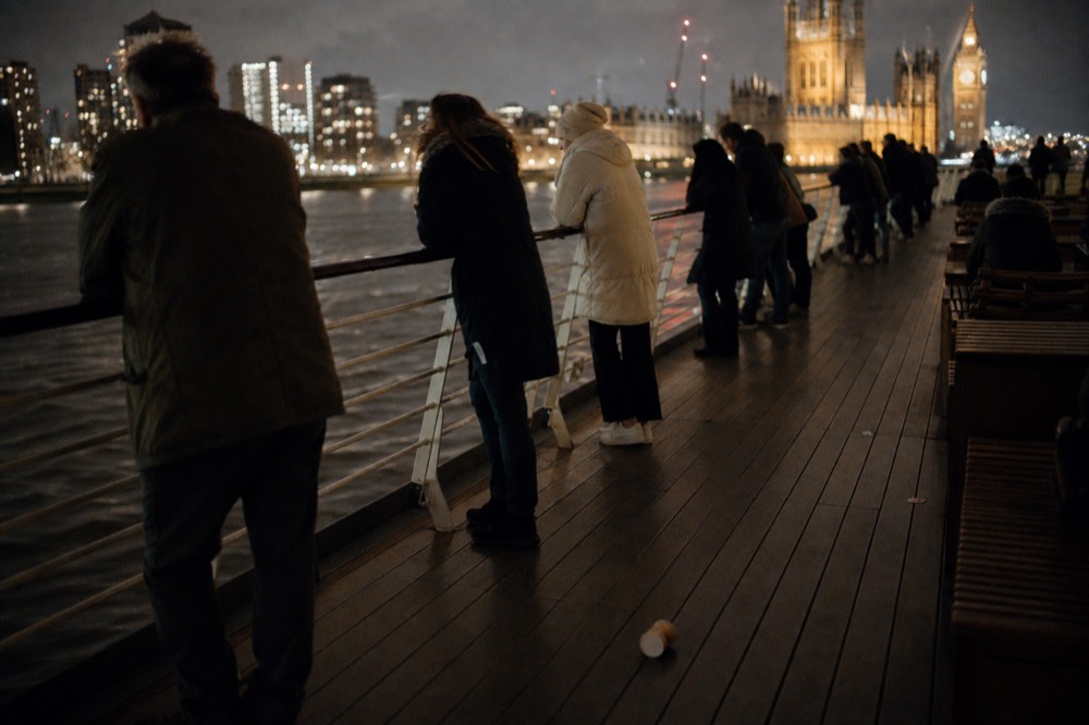 Passengers on an open deck watching the illuminated Budapest riverfront from a cruise boat, no text, no logos, no people.