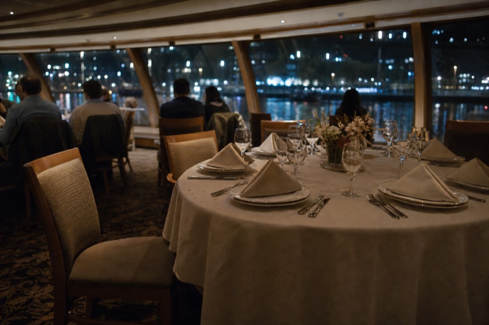 Dinner table set on a Danube cruise boat with city lights through the window, no text, no logos, no people