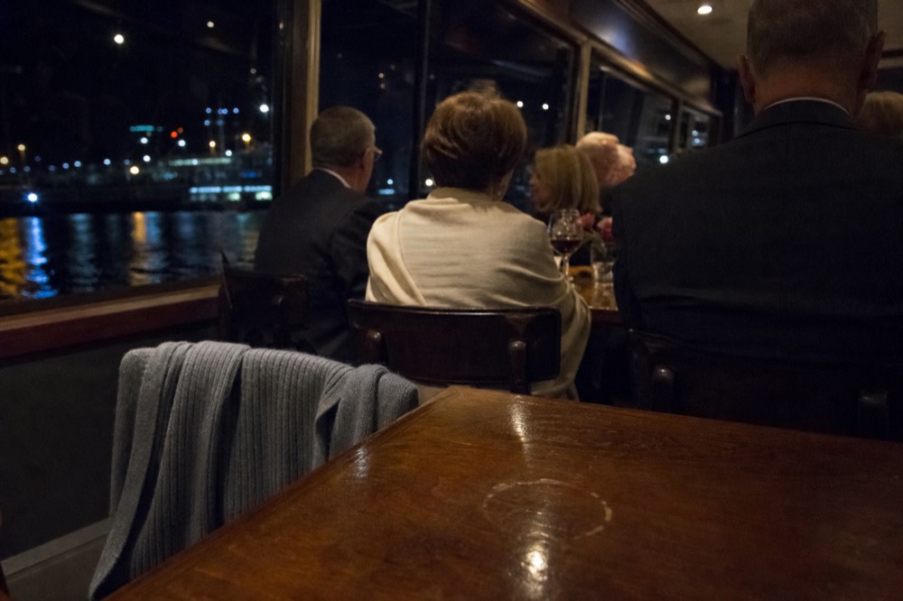 Passengers in smart-casual clothes enjoying a night cruise dinner with city lights outside, no text, no logos, no people