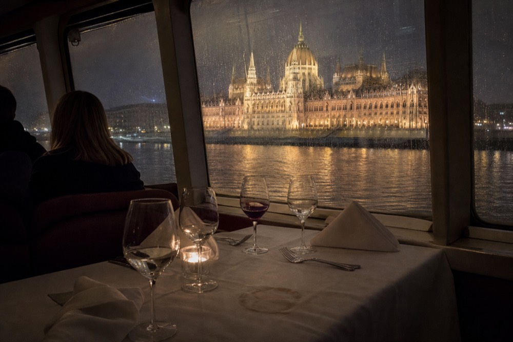 A set dinner table on a river cruise boat with the illuminated Danube banks outside, no text, no logos, no people