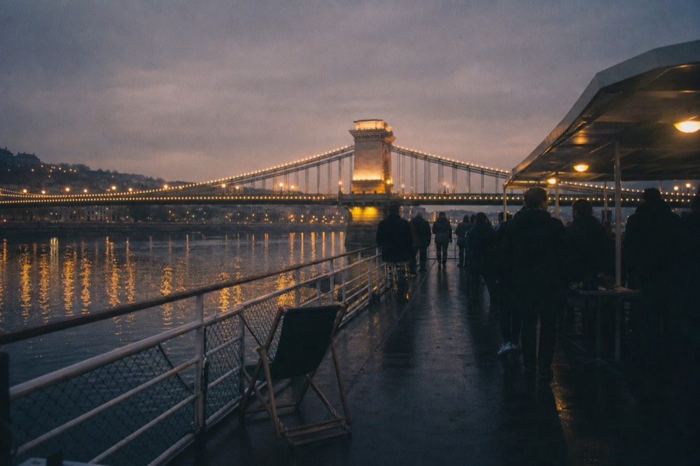 A cruise boat on the Danube at dusk with the Chain Bridge lit in the background, no text, no logos, no people
