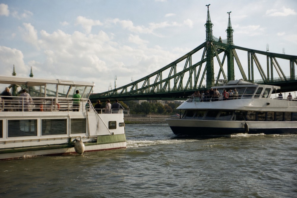 Two river cruise boats passing on the Danube with the Liberty Bridge in the background, no text, no logos, no people