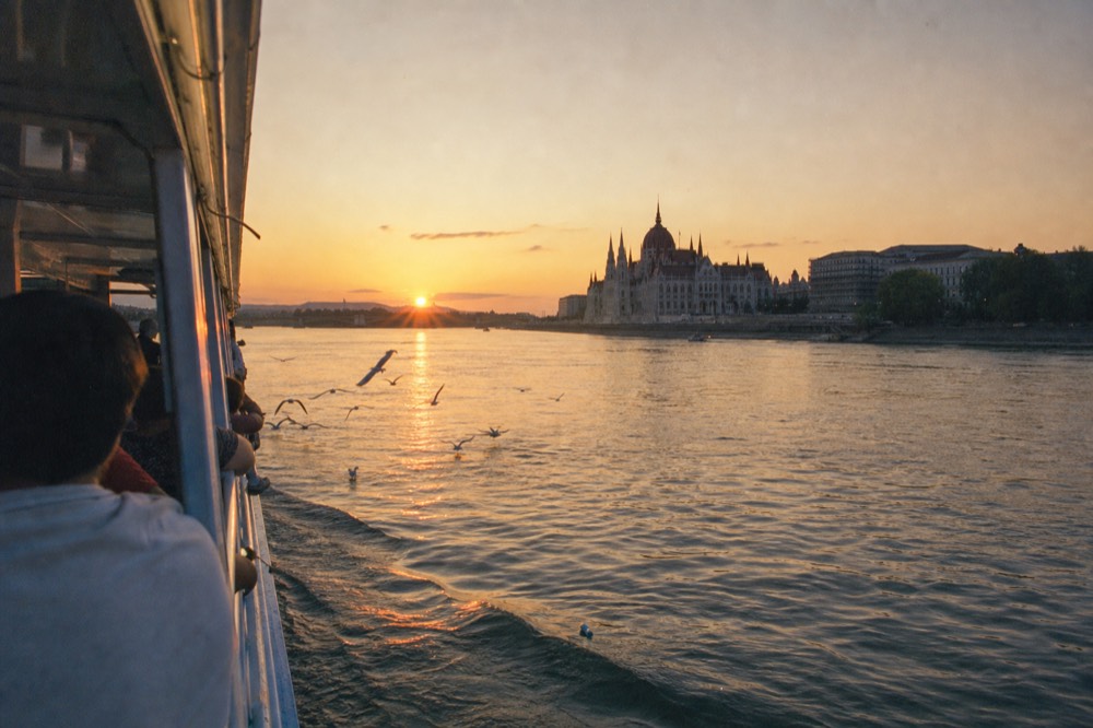 Sunset over the Danube with a sightseeing boat heading toward the Parliament, no text, no logos, no people