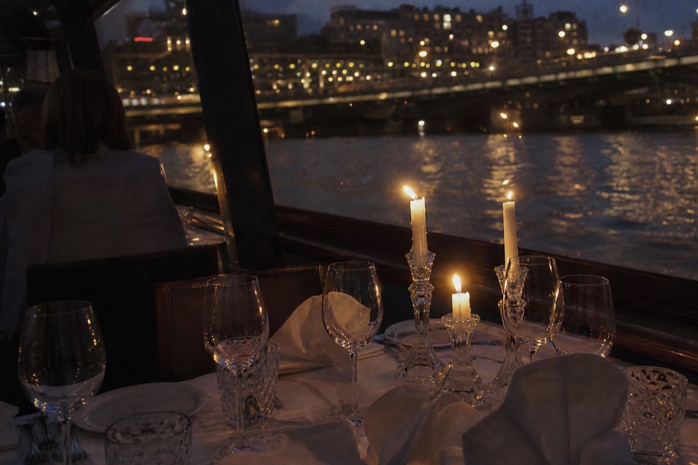 Elegantly set dinner table on a candlelit river cruise boat with city lights, no text, no logos, no people