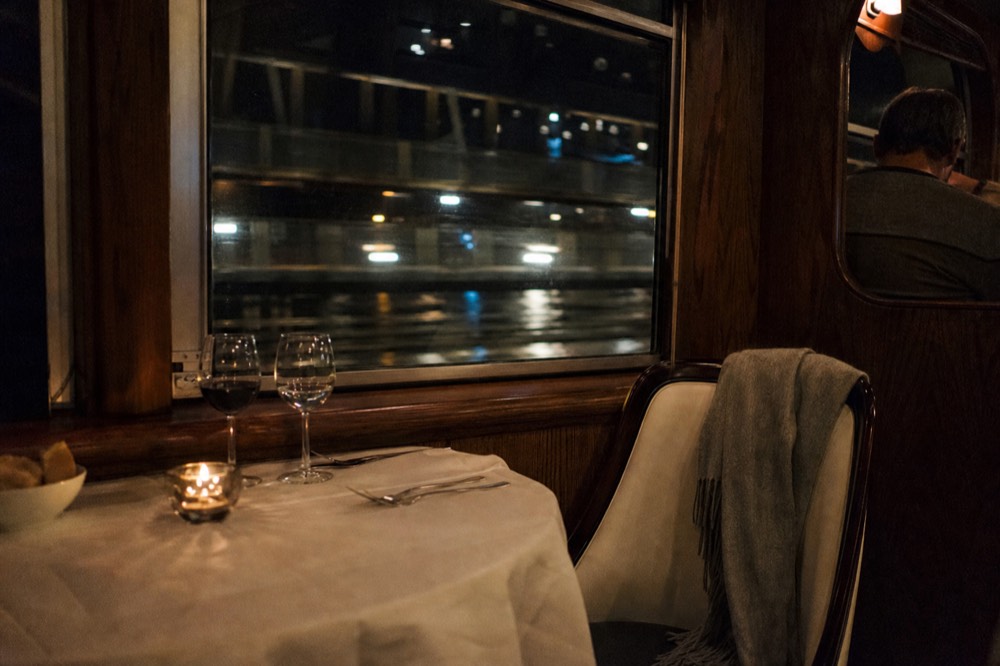 Candlelit table for two on a Danube dinner cruise with city lights through the window, no text, no logos, no people