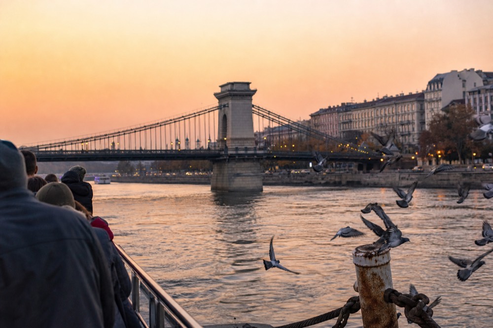 Danube river cruise boat at sunset with Budapest Parliament and Chain Bridge, no text, no logos, no people