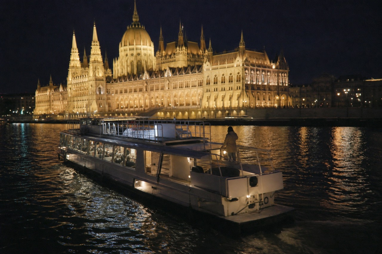 A Danube sightseeing boat passing the illuminated Hungarian Parliament building at night in Budapest